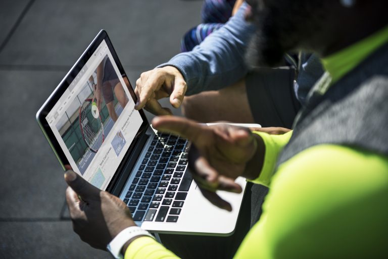 Twee sporters in sportkleding bekijken samen een sportwebsite op een laptop