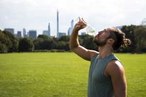 Atleet drinkt water uit een bidon tijdens een training in warm, zonnig weer