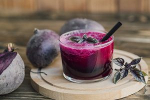 Een glas gevuld met donkerrood bietensap op een houten plankje, met een verse rode biet ernaast.